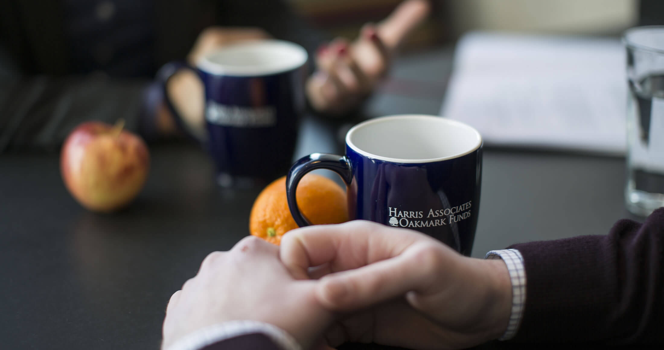 Hands on a table with oranges and a Harris-Oakmark coffee mug